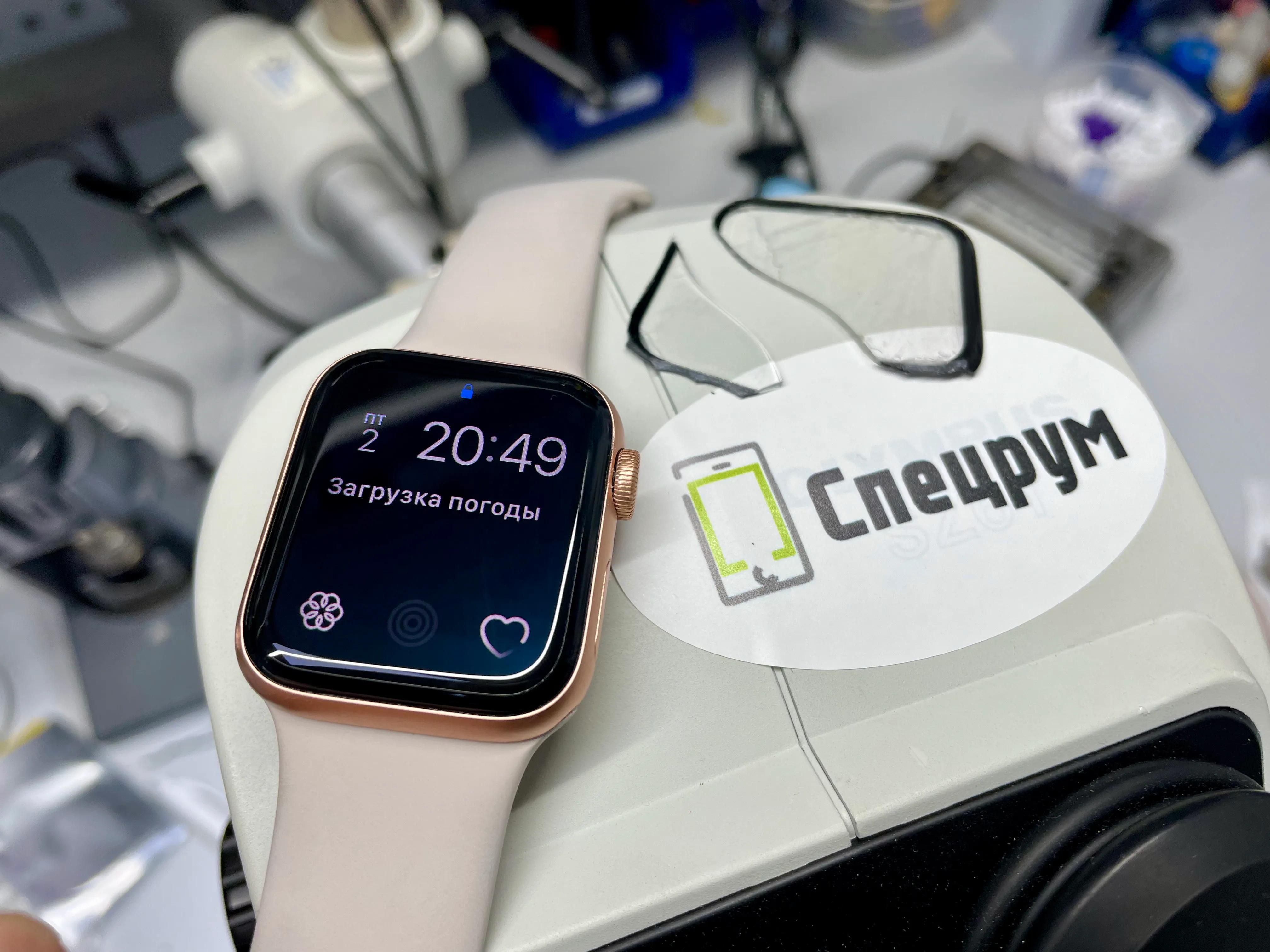 Apple Watch SE с включённым экраном, рядом повреждённое стекло и наклейка Спецрум